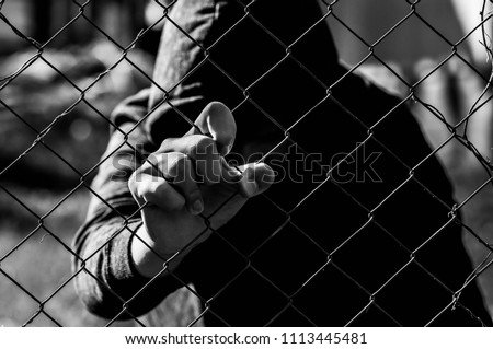 Young unidentifiable teenage boy holding the wired garden at the correctional institute in black and white, conceptual image of juvenile delinquency, focus on the boys hand. Royalty-Free Stock Photo #1113445481