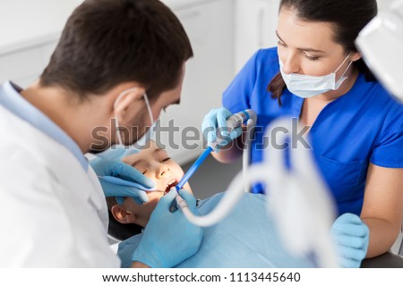 medicine, dentistry and healthcare concept - dentist and assistant with dental drill and saliva ejector treating kid patient teeth at dental clinic Royalty-Free Stock Photo #1113445640