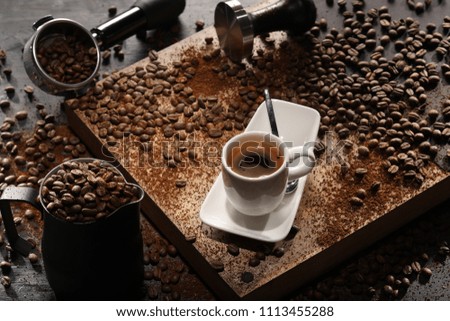 Coffee served in white cup on wooden board with coffee beans on background