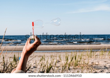 hand of young female playing with soap bubbles outdoors at beach. blowing in the wind
