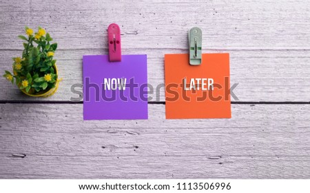 Now and Later text on sticky notes over wooden background. Decision making concept