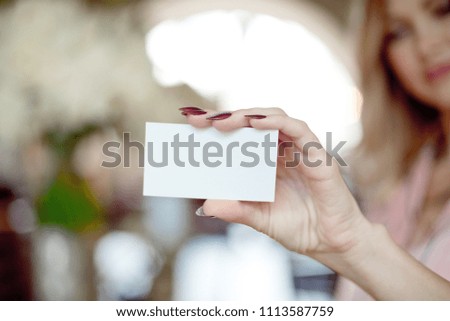 Female hand with neat manicure holding white empty blank business card on beautiful blurred background with bokeh.