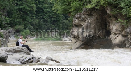 Young man takes pictures on the bank of a stormy river. Sunny summer day