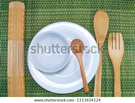 picture with a set of kitchen utensils plates of earthenware spoons and bamboo paddles and a mat to prepare sushi all on a green background