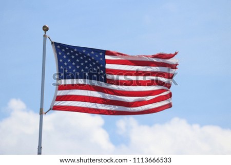 American flag flapping flying in the wind in a blue sky.