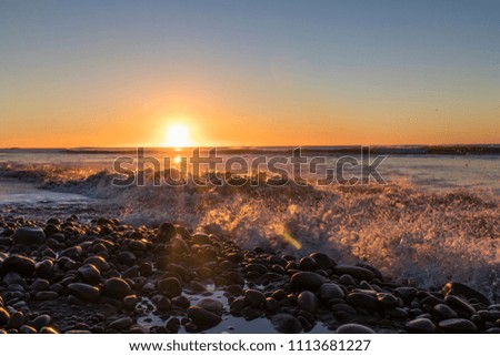 Sun setting into sea behind crashing waves