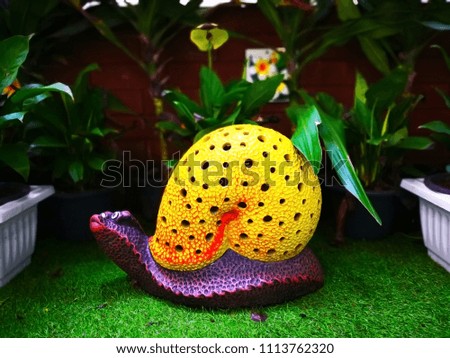 The colorful ceramic snail with yellow shell and purple body, which is on green artificial grass and decorated in a public small park. Selective focus and copy space.