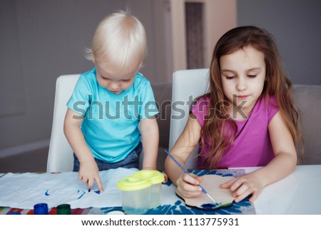 Two happy children Blond boy and girl drawing paints and brushes and sitting at table at home.