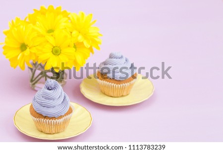 Cupcakes decorated with violet cream and bouquet of yellow chrysanthemums on violet pastel background. Text area. Ideal for greeting, mothers days and valentines card. Minimal still life concept.