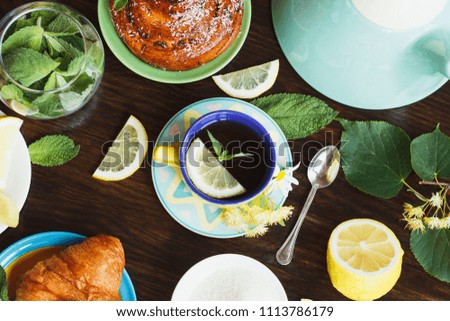 Cup of herbal tea with lemon and mint leaves, ginger root and croissant on the wooden background, top view