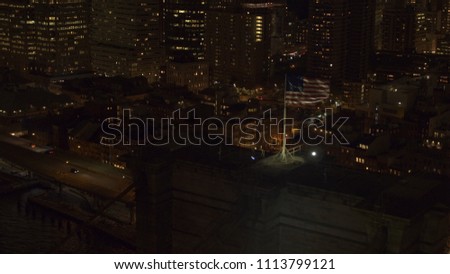 AERIAL: American flag waving in the wind on iconic Brooklyn Bridge lit at night