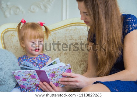 Young mother and her baby daughter looking photobook togerher at home. Family, childhood and leisure concept