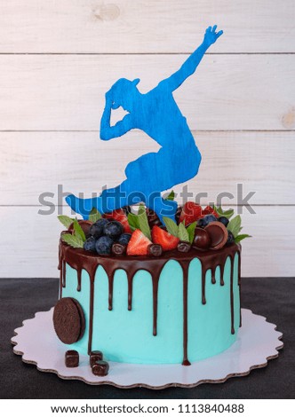 a beautiful homemade cake with green cheese cream, strawberry and cherry berries, decorated with a figure of a dancer in a hat, on a wooden background