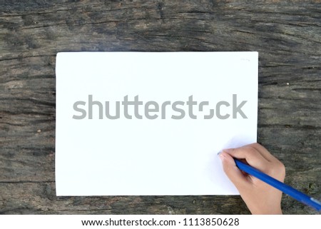 HANDS HOLDING A PEN WITH BLANK WHITE PAPER OVER WOOD PLATE BACKGROUND