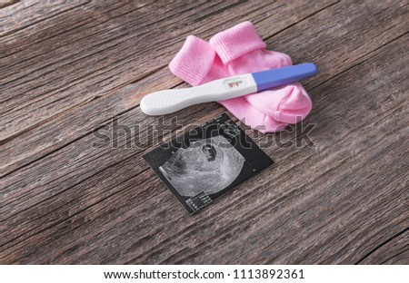 Pregnancy test and baby socks picture of the embryo. On a wooden background.