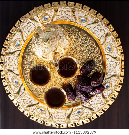 Traditional golden arabic coffee set with dallah, three cups of tea and dates. Dark background. Square image. Top view.