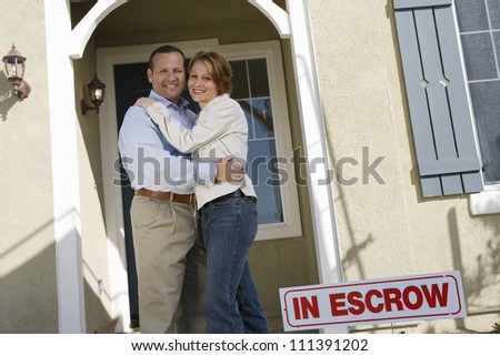 Happy middle aged couple embracing in front of house for sale