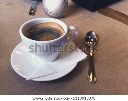 Breakfast in the cafe. Cup of Americano coffee in white mug, saucer and spoon. Close-up photo.