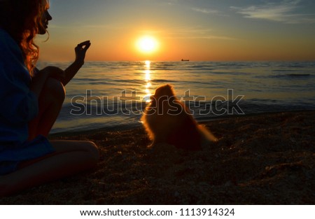 A girl is training a dog on the beach at sunset