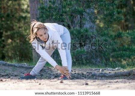 Young slim woman in sportswear stretching outdoors during a run in pine woods on a sand beach, sunny morning, active lifestyle concept, copyspace
