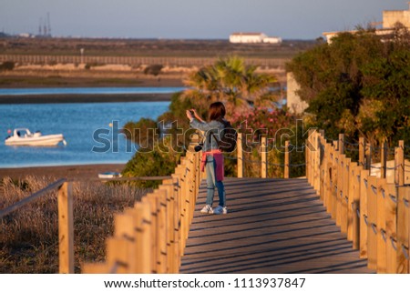 Sunset view of a tourist photographing beach landscape over a wooden path.