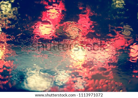 Abstract blurred Light traffic jam bokeh from inside a car view to outside road background while raining with rain drops on glass, night cityscape,cinematic photography vintage with film grain style.