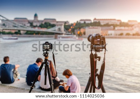 Cameras on tripods photograph a bridge and a river in the city of Budapest. Concept training and Workshop or masterclass on landscape and city photography.
