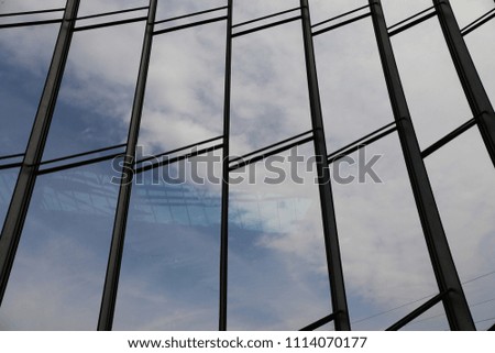 Inside view of transparent glass windows. Blue cloudy sky in background. Graphic image with vertical and horizontal steel lines composing rectangular shapes. Abstract design of a building facade. 