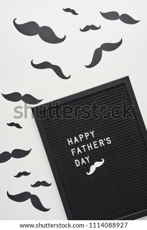 Black letterboard with white plastic letters with quote Happy Father's Day, on white background with mustache.