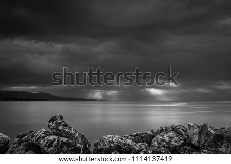 Dramatic sunburst through heavy stormy hurricane rain clouds beyond the coastline mountains. Black and white edit.