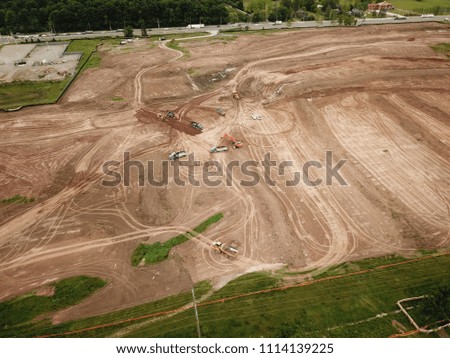 Aerial drone image (top view) of a construction site.  Heavy equipment is grading the land, moving and flattening out red clay soil.