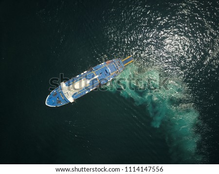 Aerial drone image of a large ferry turning slowly in a Mediterranean green harbour.