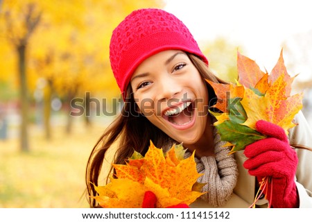 Excited happy fall woman smiling joyful and blissful holding autumn leaves outside in colorful fall forest. Beautiful energetic mixed race Caucasian / Asian Chinese young woman.