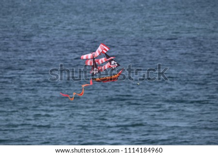 American flag pirate ship kite flying over blue sky and ocean water.