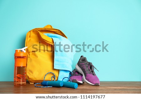 Sports bag and gym equipment on wooden floor against color background Royalty-Free Stock Photo #1114197677