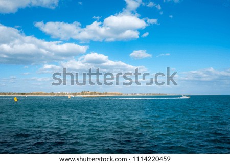 Bright sunny day at blue sea with cloudy blue sky and a view of fast moving boat on the waters.