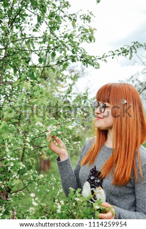 Portrait of a beautiful redhead girl in the spring garden. Young woman wearing in grey jumper with owl. Pink nad white flowers. Smiling positive healthy people. 