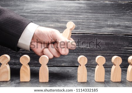 The hand of a businessman grabs a wooden figure of a man from a number of workers. The concept of business management, human resources. Specialists, career growth. Dismissal of the employee.