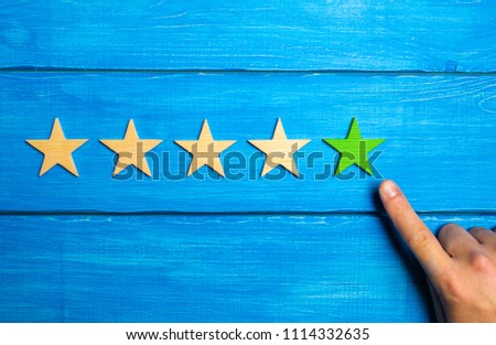 The male hand points to the fifth green star on a blue wooden background. Five Stars. Rating of restaurant or hotel, application. Evaluation of quality and service, critical evaluation.