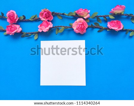 Paper note and rose flowers on blue background with copy space.