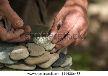 closeup of hand of man making stones balance on wooden table on green blurred background 