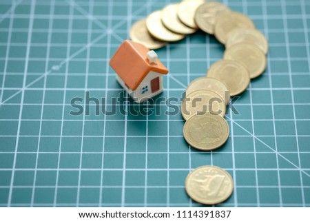 Mini house with question mark pattern coins on green background.  Concept of Investment Property. 
