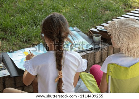 two girls are sitting in the park and painting with watercolor.