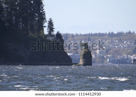 A view of Siwash rock as seen from across the bay.  you can see people walking on the sea wall around Stanley Park taking advantage of the sunny day