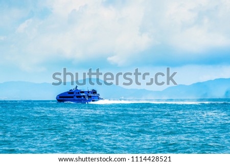 High speed water jet passenger nautical vessel moving fast from Hong Kong to Macau (Asian gambling center). Sunny day, cloudy sky. Blue hills on horizon line. Foaming wave trace behind the ferry.  Royalty-Free Stock Photo #1114428521