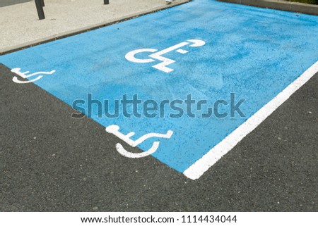 International handicapped symbol painted in bright blue on a shopping center parking space. The space is clearly marked on either side with additional white diagonal stripes