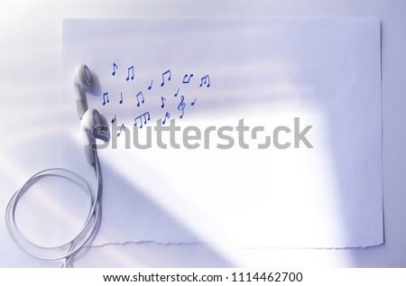 white little headphones and music notes on paper background. minimal creative concept of digital music. atmosphere composition. copy space. flat lay