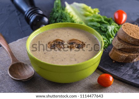 Cream of mushroom soup in a green bowl on the table. Dark background. Healthy autumn vegetarian traditional dish