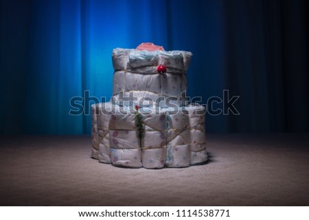Newborn gift concept. Cake of diapers. Wrapped diapers as cake with flowers. Cake of wrapped clean diaper on table with baby doll decorated. Selective focus.