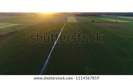 Aerial picture of countryside area during sundown early evening showing the horizon with the sun almost away also showing the meadows ans small canals between the pastures below